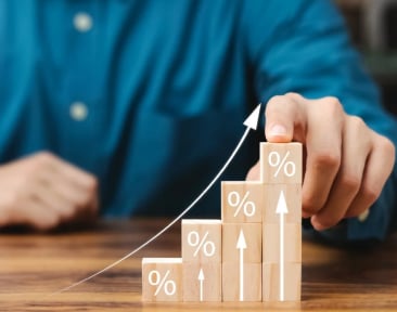 A man displays wooden blocks featuring a percentage sign, illustrating themes of finance or statistical evaluation.